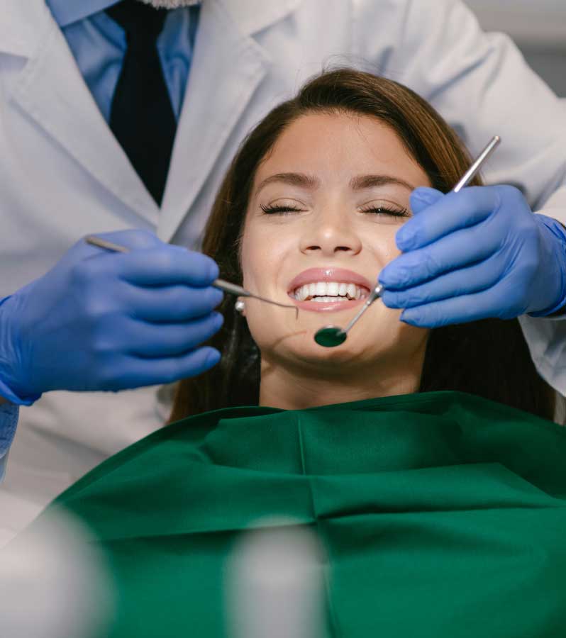 A smiling woman receiving dental treatment from a dentist who is using tools to examine her teeth