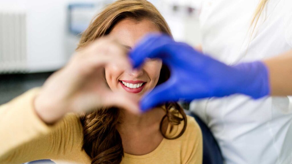 Dentist forming a heart shape with hands around a smiling patient's face