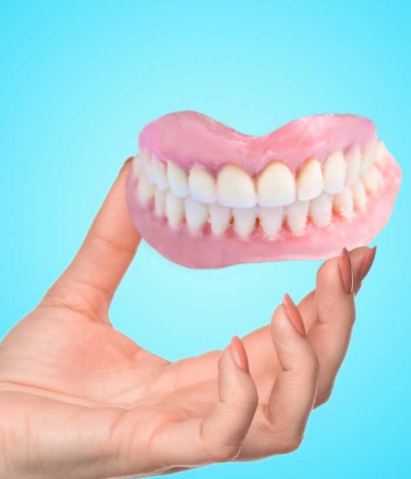 A-hand-holding-a-full-set-of-upper-dentures-against-a-vibrant-blue-background