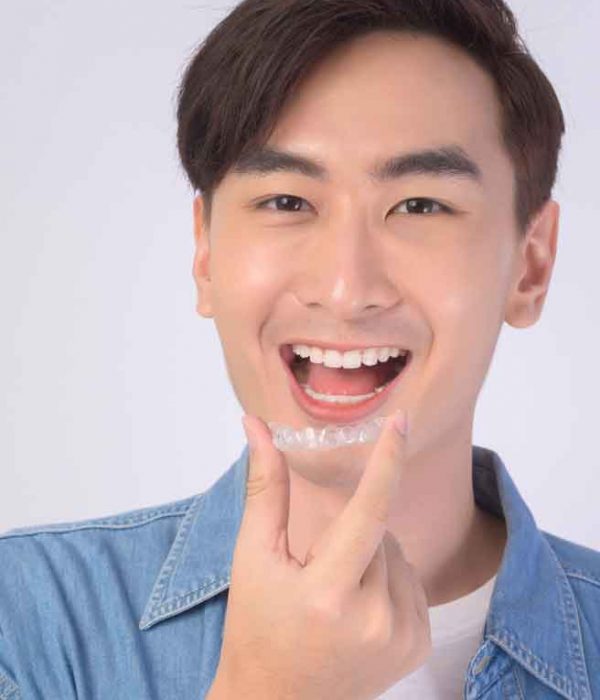 A man visibly smiling while holding his invisalign brace