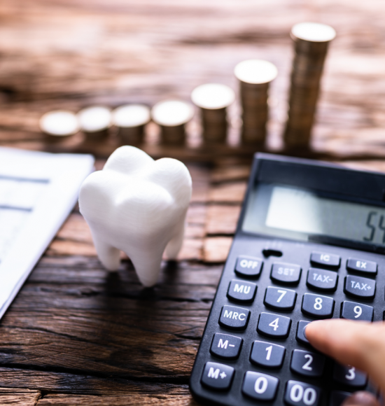 A person’s hand holding a pen over a financial document, next to a large model of a molar tooth