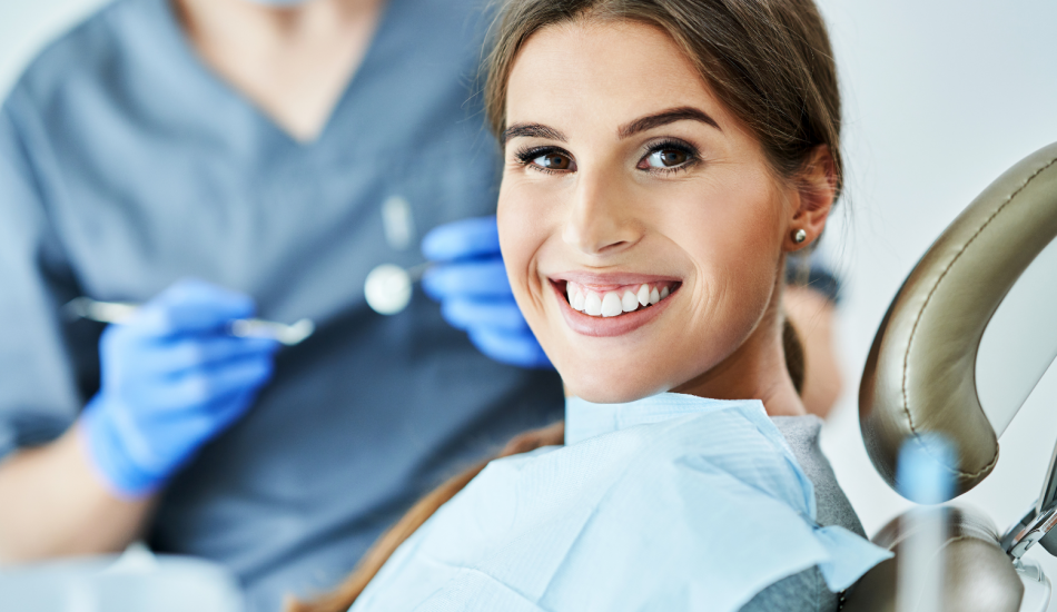 A woman smiling in a dental chair with a dentist in the background